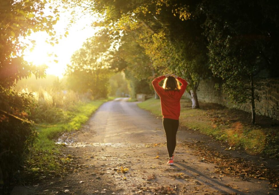 A woman is walking down the road in the sunlight.