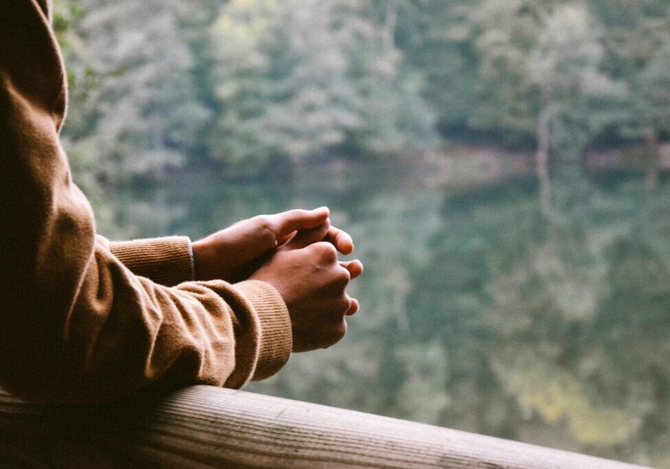 A person with their hands clasped together on the side of a bridge.